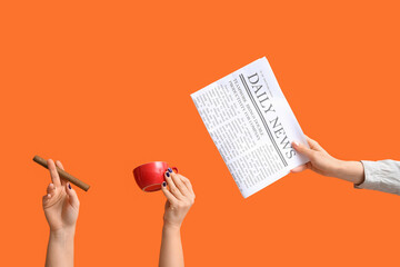Female hands with newspaper, cup of coffee and cigar on orange background