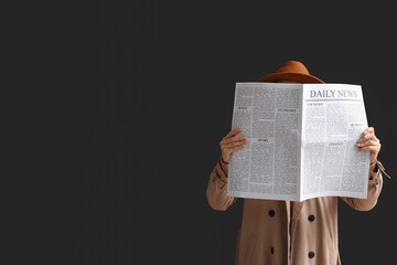 Woman in cloak and hat with newspaper on black background
