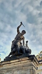 Stone Sculpture Man Stabbing Figure with Knife under Dramatic Clouds