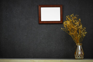 Hanging empty picture frame mockup and gypsophila flowers vase on wooden table near grunge wall,...