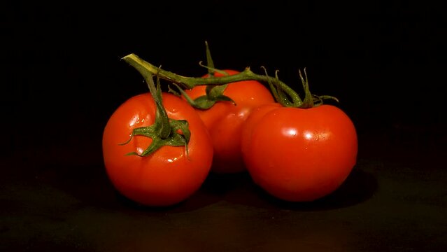 Close-up footage of red tomatoes with green stems on black background.