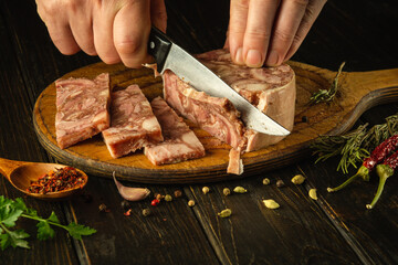 Slicing headcheese on a kitchen board before setting the table in a restaurant for dinner. Knife in the hand of a chef while cutting brawn.