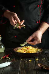 A professional chef adds rosemary to a bowl of pasta for flavor and aroma. Work environment in...