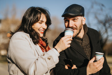 Two joyful professionals taking a coffee break outside on a bright winter day, exuding warmth and...