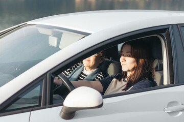 Naklejka premium A young girl learns to drive a car with her mother in the passenger seat as the sunlight illuminates their smiling faces.