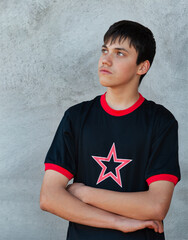 teenager boy with the arms crossed in front of him, outdoors wall as a background