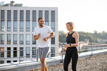 Young sports couple doing sports in morning on roof of modern building. Happy man and woman jogging...