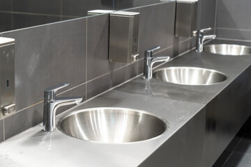 A row of metallic toilets in a gray tiled public toilet	