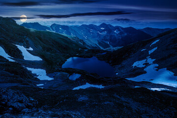 glacier lake among rocky hills at night. mountainous landscape in full moon light