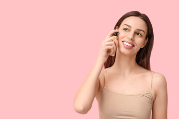 Beautiful young woman applying foundation on pink background