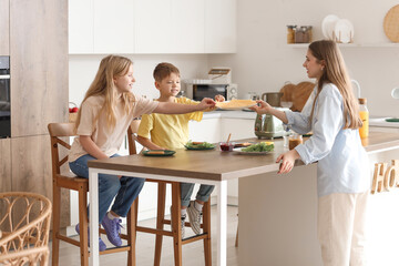 Little children and their mother making toasts with cheese in kitchen