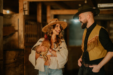 Smiling young rancher couple with chicken in hands at barn.