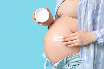 Pregnant woman applying body cream against color background, closeup
