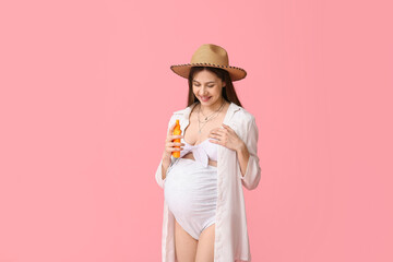 Beautiful young pregnant woman in swimsuit with bottle of sunscreen cream on pink background