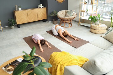 Little girl with her mother doing yoga on mats at home