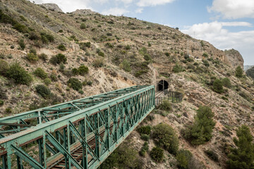 green railway train track bridge and tunnel. Hiking trail caminito del rey, kings walkway, El Chorro Spain. narrow footpath leads through natural beauty mountain range cliff faces of gaitanes gorge. 