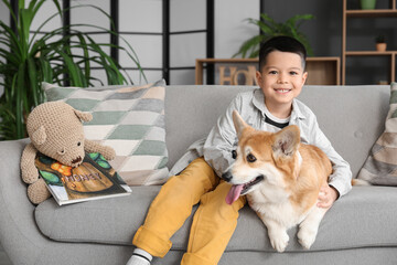 Little happy Asian boy with cute Corgi dog and book sitting on sofa at home