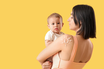 Young mother with her little baby and sun made of sunscreen cream on yellow background