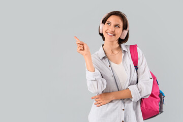 Happy female student with backpack and headphones pointing at something on white background