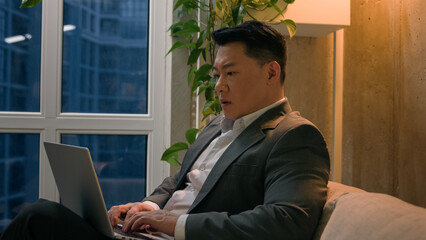 Asian man korean chinese japanese middle-aged businessman working remote internet typing laptop writing business project in office company male employer use computer indoors sad shocked stress upset
