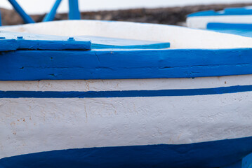 A blue and white boat with a white stripe. The boat is sitting on the ground. The boat is old and has a rustic look - Powered by Adobe