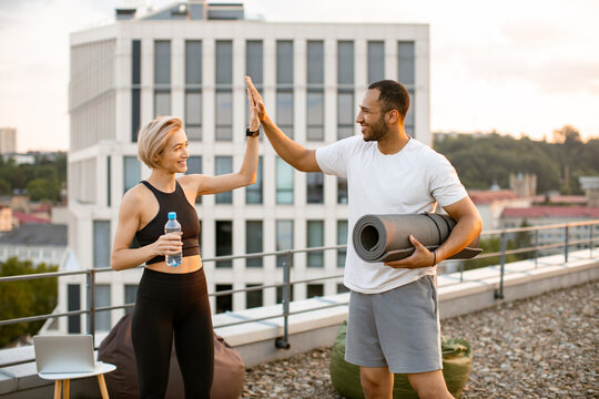 Happy sports couple giving each other high five after completing sports workout on rooftop against urban background. Cheerful husband and wife celebrate end of physical morning warm-up. - Powered by Adobe