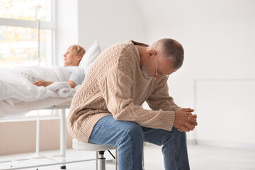 Sad mature man and his wife lying in clinic