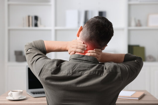 Man suffering from neck pain at table, back view