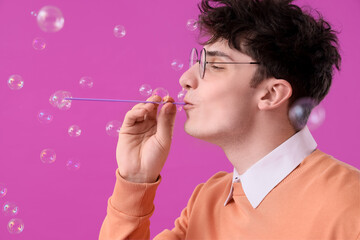 Male student blowing soap bubbles on purple background, closeup
