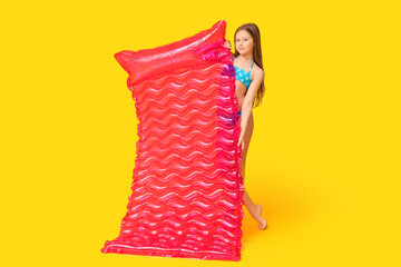 Cute little happy girl in swimsuit with inflatable mattress on yellow background