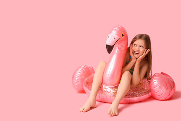 Cute little happy girl in swimsuit with inflatable ring sitting on pink background