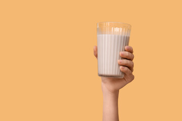 Female hand with glass of sweet chocolate milk on yellow background