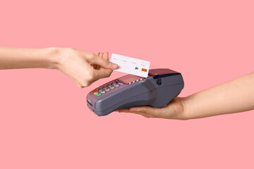 Woman with credit card paying via payment terminal on pink background