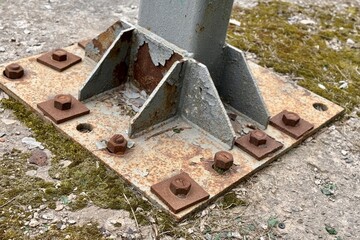 Metal pillar fastened to basement with anchor bolts and nuts. The rusty surface of the post and the fastenings are in places. The support of the iron pillar on a green lawn in the park. Close-up