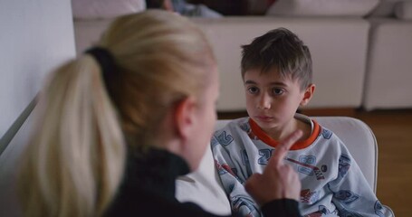 A mother is seen reprimanding her young son, who appears attentive and possibly remorseful, in the familiar environment of their home.