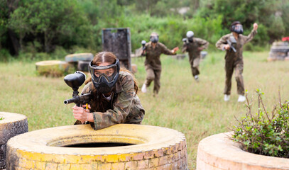Female paintball player in protective mask with ammunition and gun on paintball field