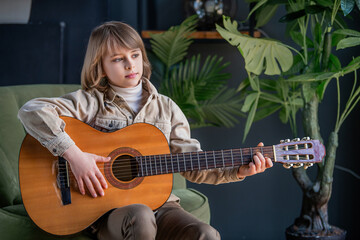 A young boy is sitting on a green chair and playing a guitar.