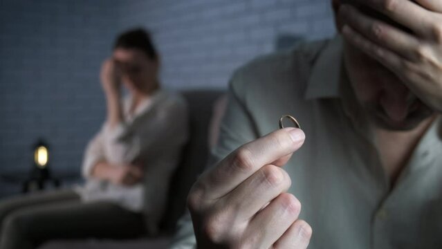 Upset husband during lovers conflict. A depressed man with a wedding ring with an offended woman in the background.