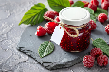 Glass jar with raspberry jam and a white label arranged by raspberries