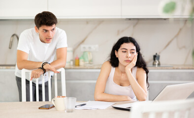 Obraz premium Young guy screams during family quarrel with young woman using laptop in kitchen