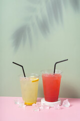 Coloured lemonade drinks in takeaway glasses on coloured background with palm shadow