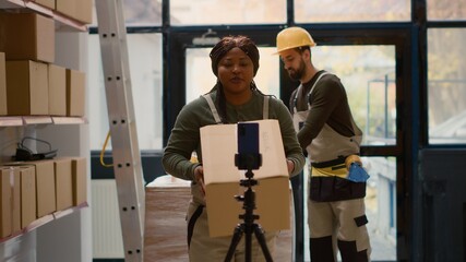 Warehouse supervisor pressing play on cellphone placed on tripod to start recording training video...