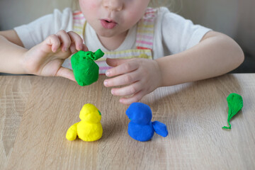close-up plasticine toys in hands of toddler, small child, blonde girl 2 years old sculpts figures...