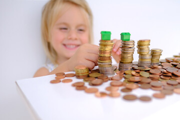 small child, blonde girl 3 years old playing with cash, house model on stacks euro currency coins,...