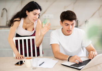 Obraz premium Young woman screams during family quarrel with young guy using laptop in kitchen