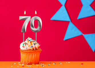 Number 70 candle with birthday cupcake on a red background with blue pennants