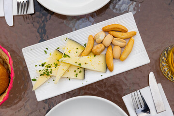 Slices of semi-hard spanish manchego sheep cheese sprinkled with chopped herbs and crutones at...