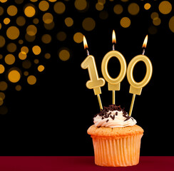 Number 100 birthday candle - Cupcake on black background with out of focus lights