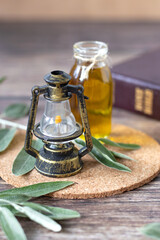 Rustic lamp and bottle with olive oil on wooden table with green tree branch and holy bible book in...