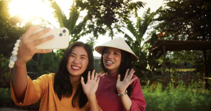 Smiling happy girls blogger vlogger wearing elegant traditional dress and hats speaking looking at camera talking make video conference call record blog vlog doing video chat a background of tropics